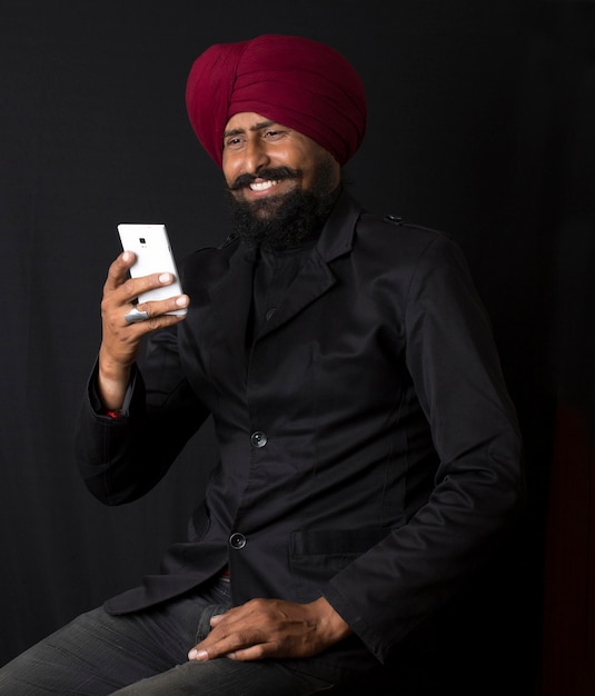 Portrait of smiling authentic native indian punjabi sikh men in turban with bushy beard, talking on mobile