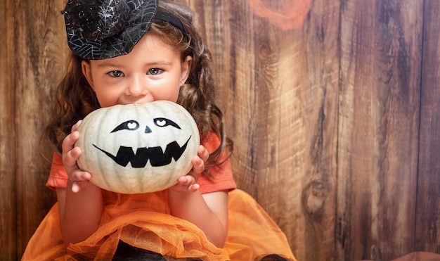 Foto ritratto di bambina sorridente con zucca su fondo in legno