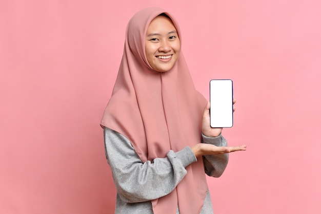 Portrait of smiling beautiful Asian muslim female showing white screen on phone