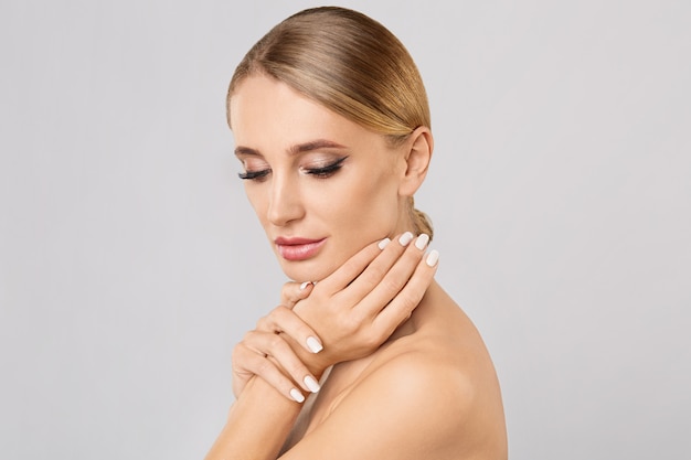 Portrait of smiling beautiful blonde woman with natural make up touching her face. 