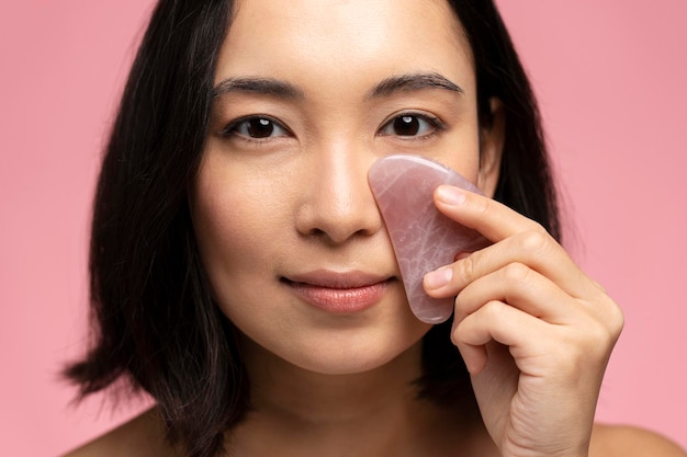 Portrait of smiling beautiful naked asian woman using facial gua sha jade board