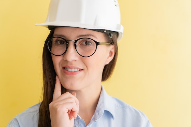 Portrait of smiling beautiful tatar woman engineer in construction helmet and glasses isolated on yellow background