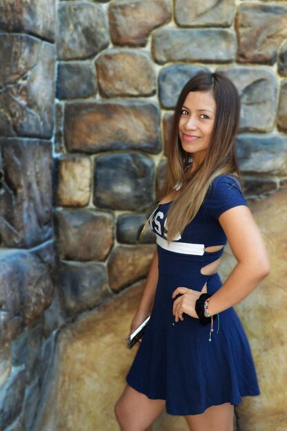 Portrait of smiling beautiful woman standing against wall