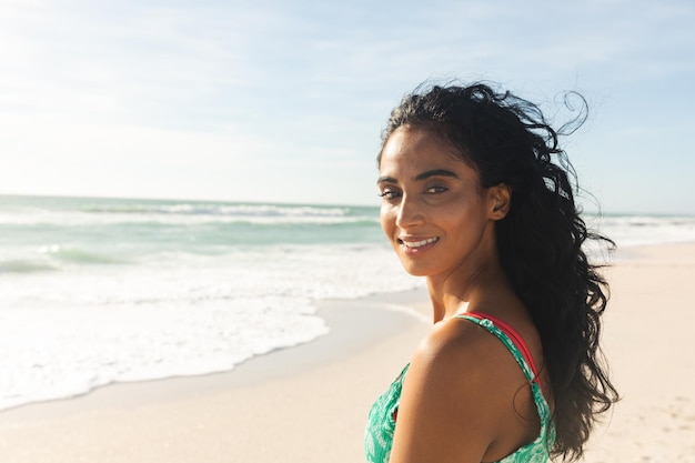 Portrait of smiling beautiful young biracial woman looking over shoulder at beach enjoying sunny day