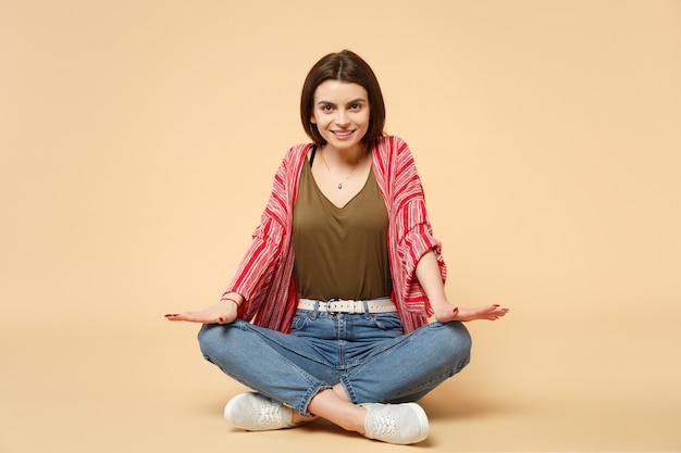 Ritratto di bella giovane donna sorridente in vestiti casuali che si siedono, guardando la macchina fotografica isolata sul fondo beige pastello della parete in studio. persone sincere emozioni, concetto di stile di vita. mock up copia spazio.