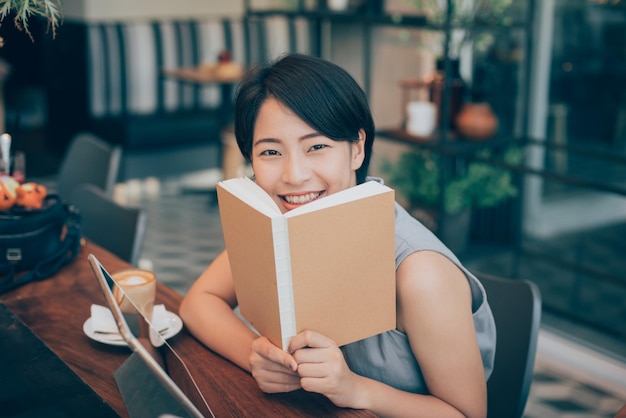 Portrait of smiling beautiful young woman holding book while sitting in cafe