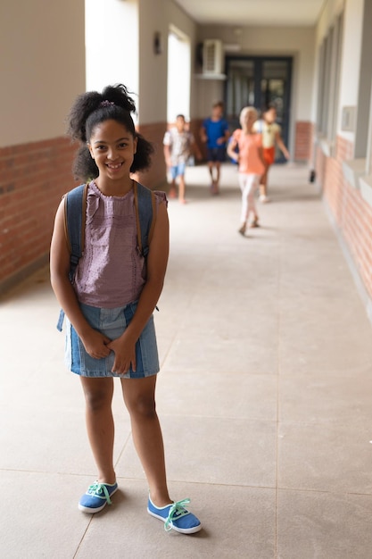 Portrait of smiling biracial elementary schoolgirl standing in corridor