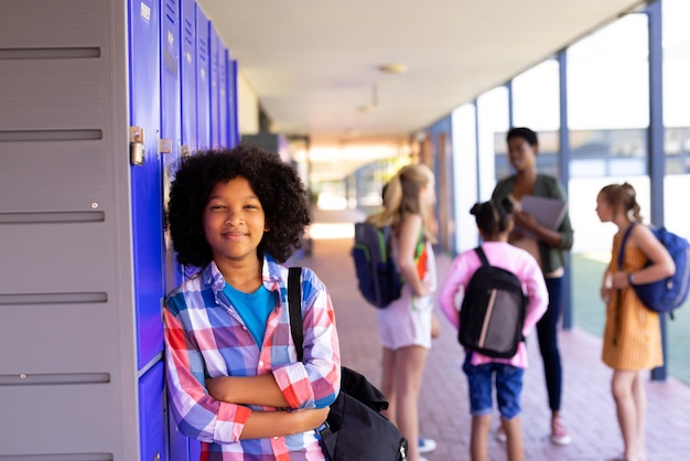 Photo portrait of smiling biracial school girl leaning on lockers in school corridor with copy space