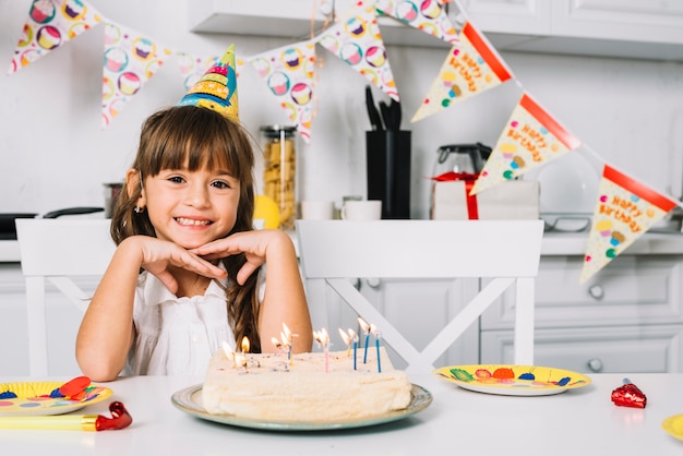 Portrait of a smiling birthday girl sitting at table with birthday cake