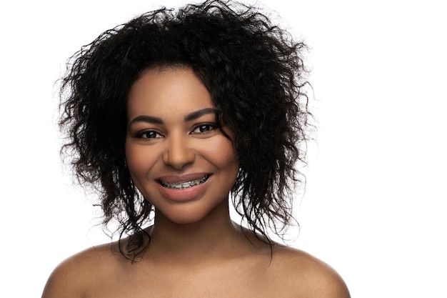 Portrait of smiling black woman with dental braces on her teeth on white background