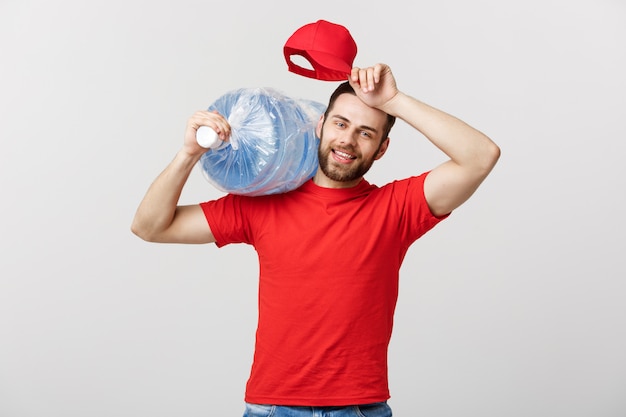 Portrait of smiling bottled water delivery courier in red t-shirt and cap carrying tank of