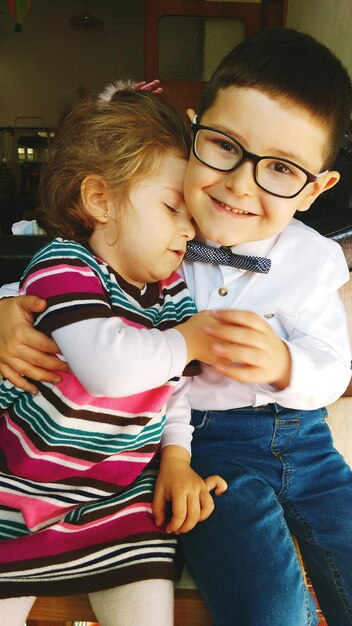 Photo portrait of smiling boy embracing sister while sitting at home