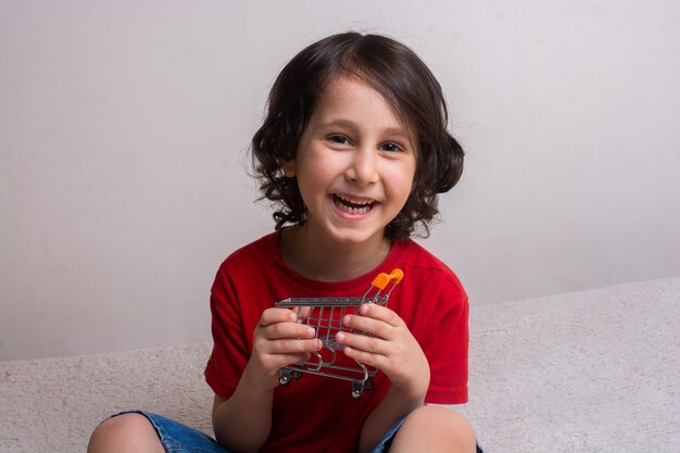 Portrait of smiling boy holding toy shopping cart against wall