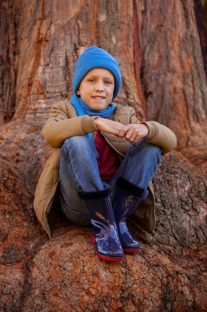 Foto ritratto del ragazzo sorridente che abbraccia le ginocchia mentre sedendosi sul tronco di albero