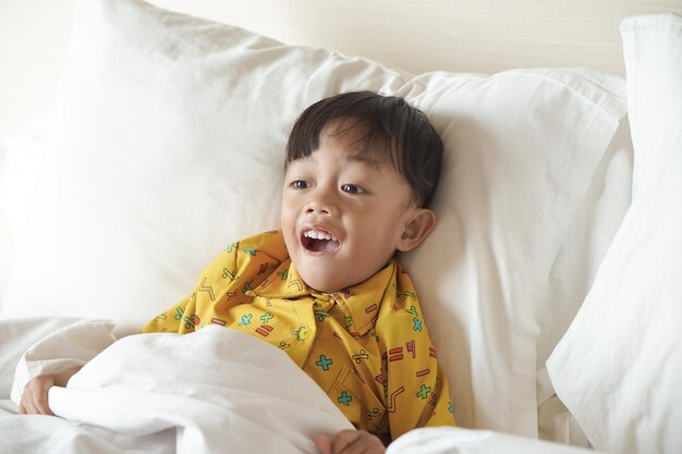 Portrait of a smiling boy lying down and wearing a blanket on the bed while watching television