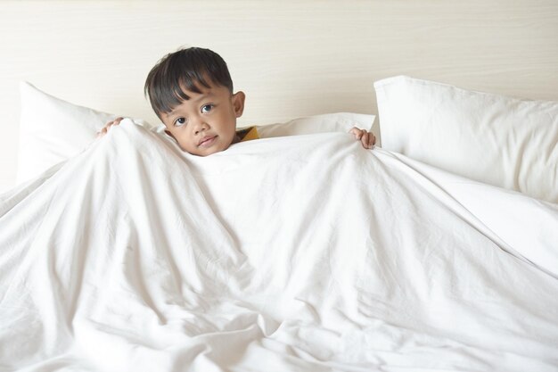 Портрет улыбающегося мальчика, лежащего и одетого в одеяло на кровати во время просмотра телевизора