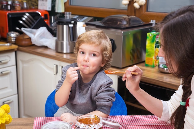 portrait of smiling boy sitting in kitchen with mother at home