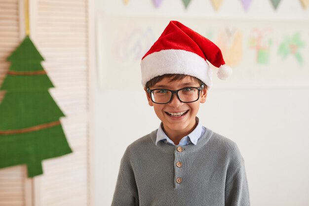 Portrait of smiling boy wearing Santa hat and looking at camera while enjoying art class on Christmas, copy space