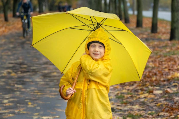 Portrait of smiling boy in yellow raincoat with large yellow umbrella in the autumn park Happy child