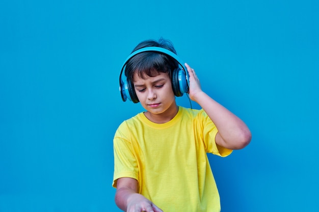 A Portrait of smiling boy in yellow t-shirt and blue headphones playing DJ