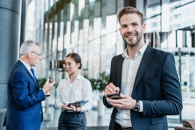 Portrait of smiling business man with smartphone in hands his collegues on background