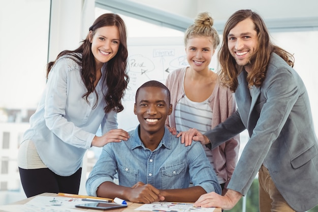 Portrait of smiling business team putting hands on man shoulder at desk 