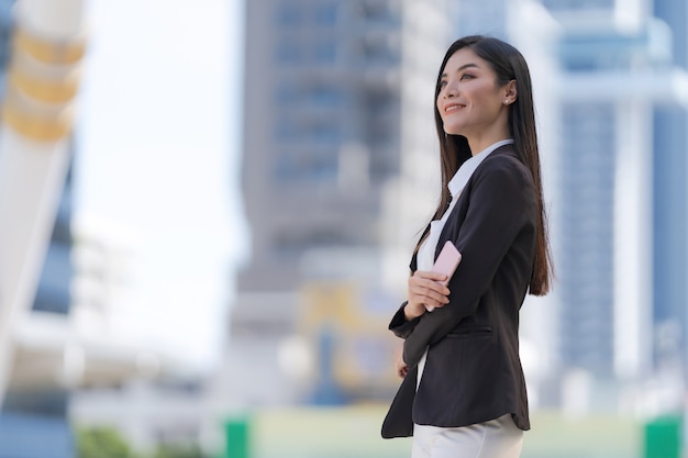 Portrait of smiling business woman holding a phone standing in front of modern office buildings