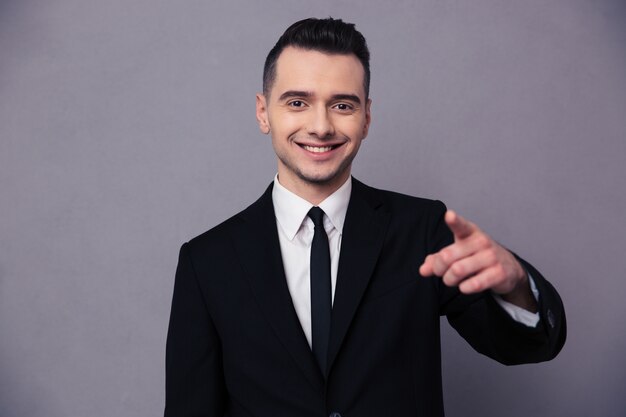 Portrait of a smiling businessman pointing finger over gray wall