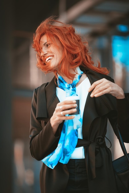 Ritratto di una donna d'affari sorridente in pausa caffè nel quartiere degli uffici in una giornata ventosa con i capelli volanti.