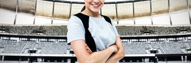 Portrait of smiling businesswoman standing with arms crossed\
against rugby goal post in a stadium front view of rugby goal post\
in a empty stadium