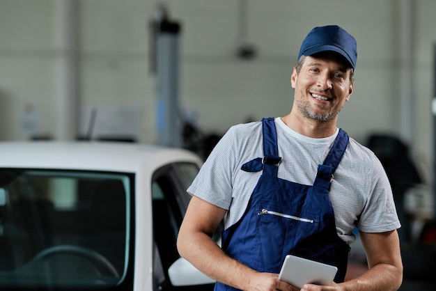 Portrait of smiling car mechanic working in auto repair shop and looking at camera