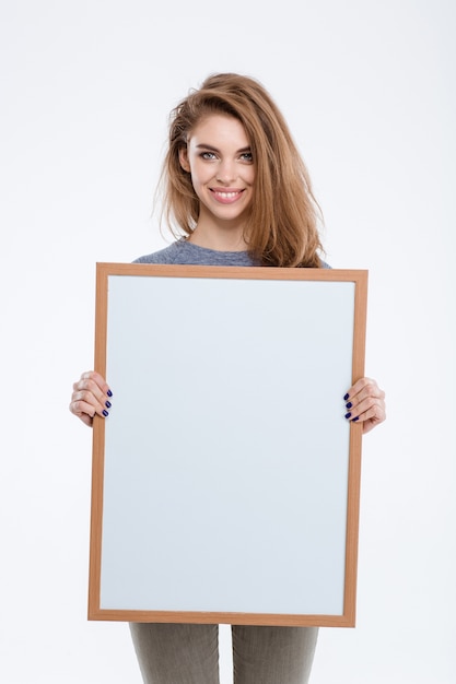 白い背景で隔離の空白のボードを示す笑顔のカジュアルな女性の肖像画