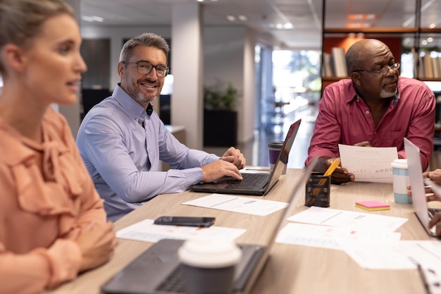 Portrait of smiling caucasian businessman sitting amidst colleagues during meeting at workplace