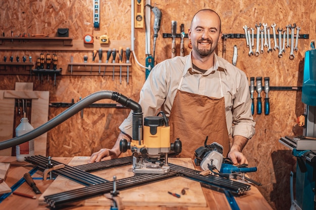Портрет улыбающегося кавказского плотника с фартуком в своей мастерской