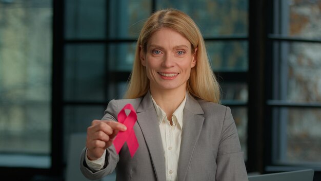 Foto ritratto di una donna di mezza età caucasica sorridente che tiene un nastro rosso posando in un ufficio moderno.