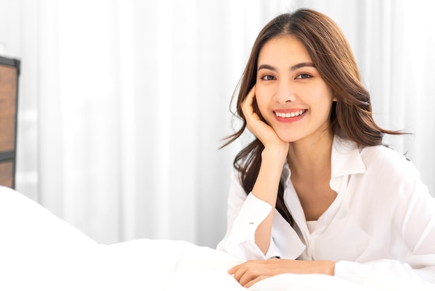 Portrait of smiling cheerful beautiful pretty asian woman clean fresh healthy white skin posing smile in pajamas white clothes.Girl felling relax and enjoy time on the bed at home.asia beauty