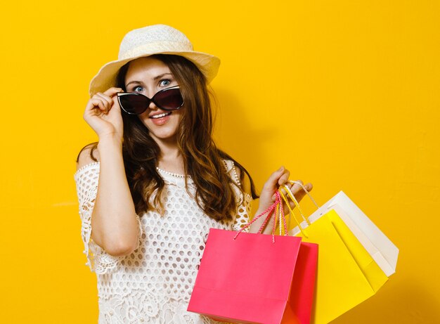 Portrait of a smiling cheerful girl holding shopping bags over yellow