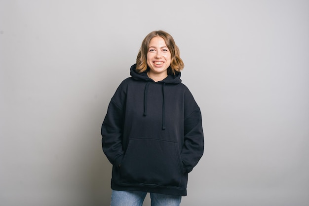 Portrait of smiling cheerful young woman in black hoodie over grey background