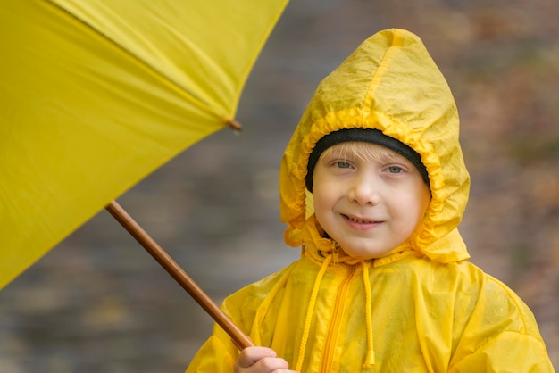 Portrait of smiling child in yellow raincoat with yellow umbrella in his hands Autumn in park