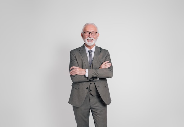 portrait of smiling confident elderly businessman with arms crossed standing on white background