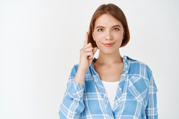 Portrait of smiling confident girl showing way pointing finger up at top promo demonstrate advertisement standing on white background