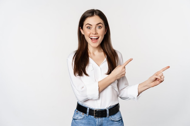 Ritratto di donna sorridente sicura di sé, ragazza d'affari che mostra pubblicità, puntando il dito verso il logo, banner o annuncio, in piedi su sfondo bianco