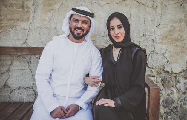 Photo portrait of smiling couple sitting on bench against wall