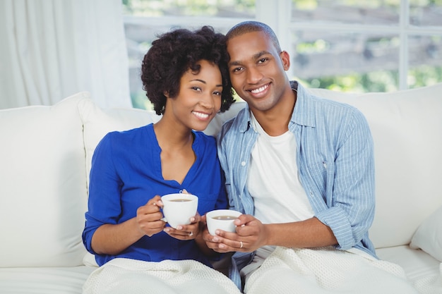 Portrait of smiling couple on the sofa holding cups