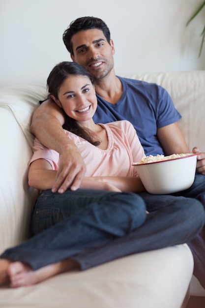 Portrait of a smiling couple watching television while eating popcorn