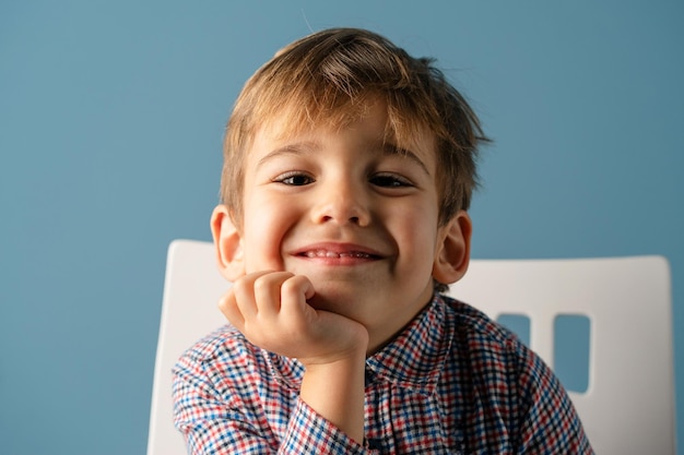 Portrait of smiling cute boy with hand on chin against blue background