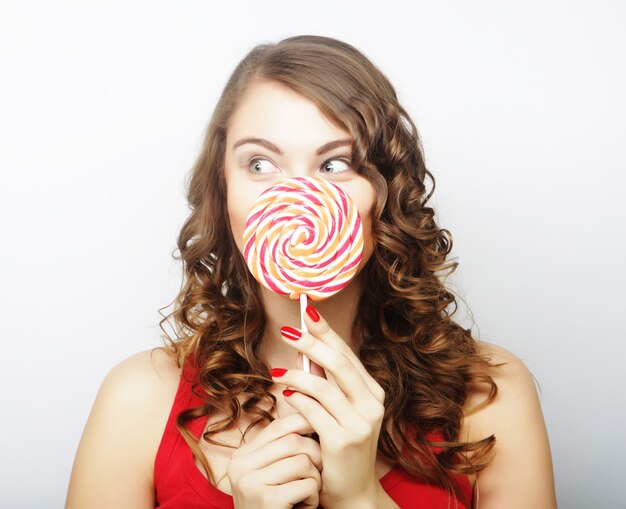 Portrait of a smiling cute girl covering her lips with lollipop over gray background