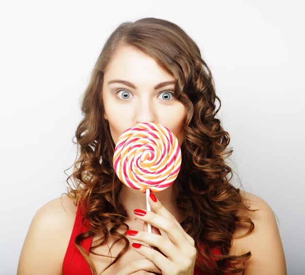 Photo portrait of a smiling cute girl covering her lips with lollipop over gray background