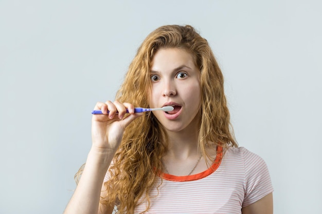 Portrait of a smiling cute woman with red curly hair holding toothbrush isolated on a white background