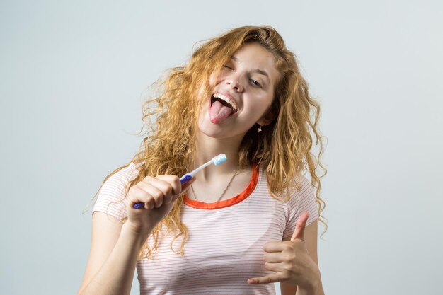 白い背景で隔離の歯ブラシを保持している赤い巻き毛を持つ笑顔のかわいい女性の肖像画